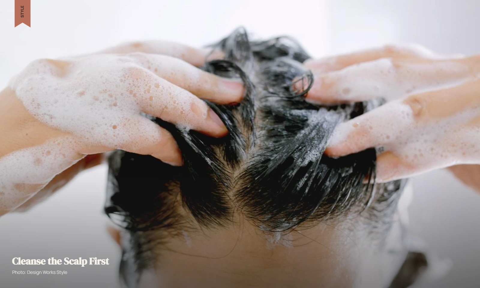 Hands gently massaging shampoo into the scalp of wet hair near the roots