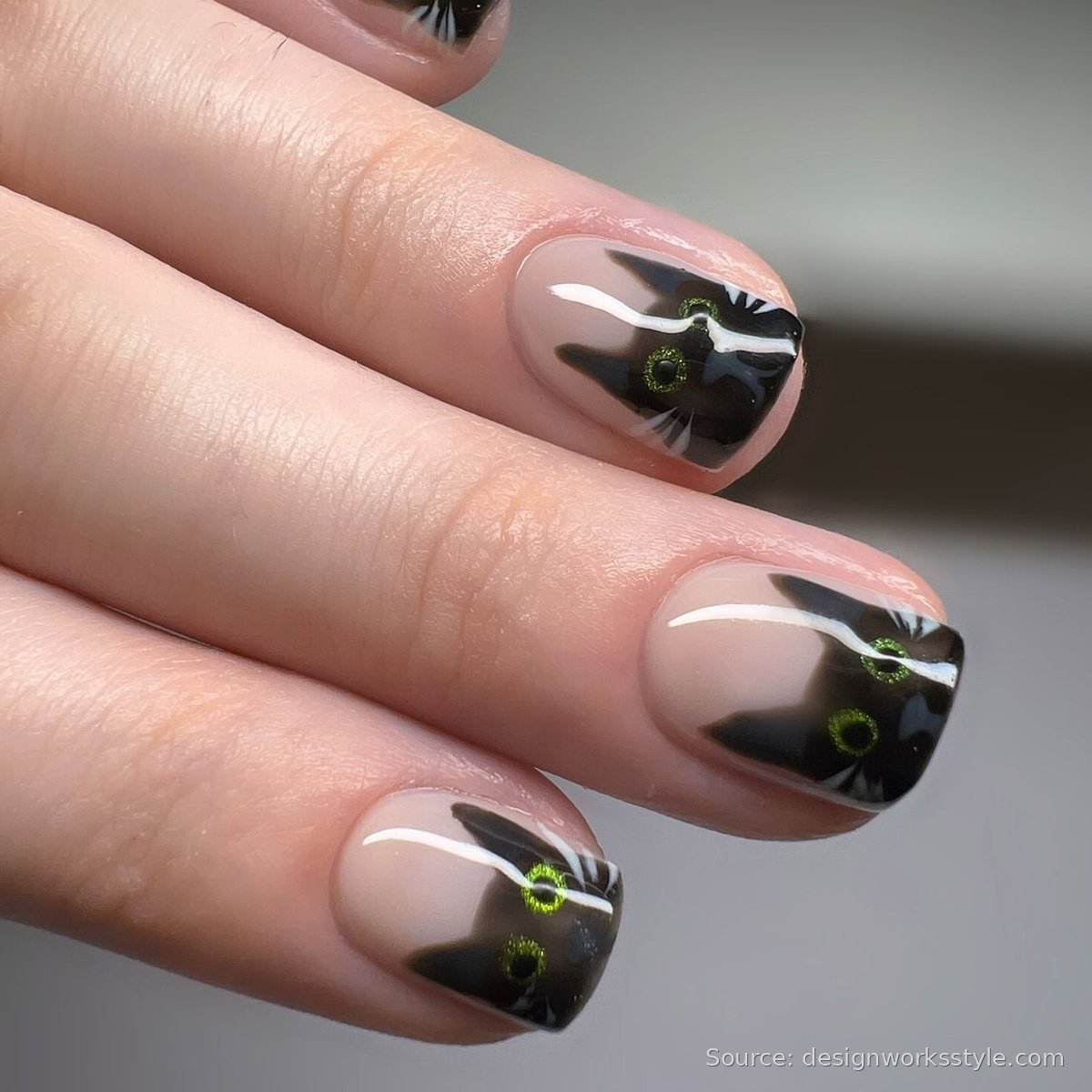 Black cat face nail art with green glitter eyes on nude French tip nails