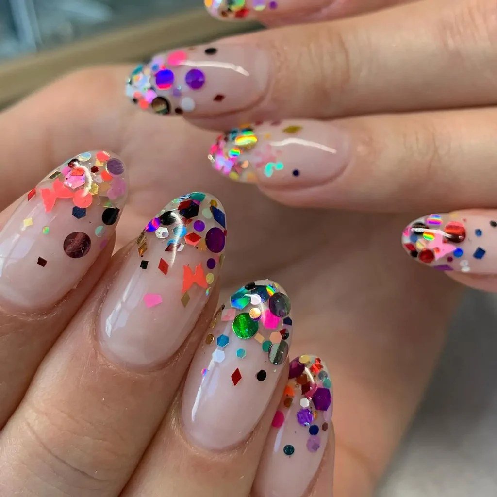 Almond-shaped nude nails covered in colorful confetti dots in pink, purple, blue, gold and black