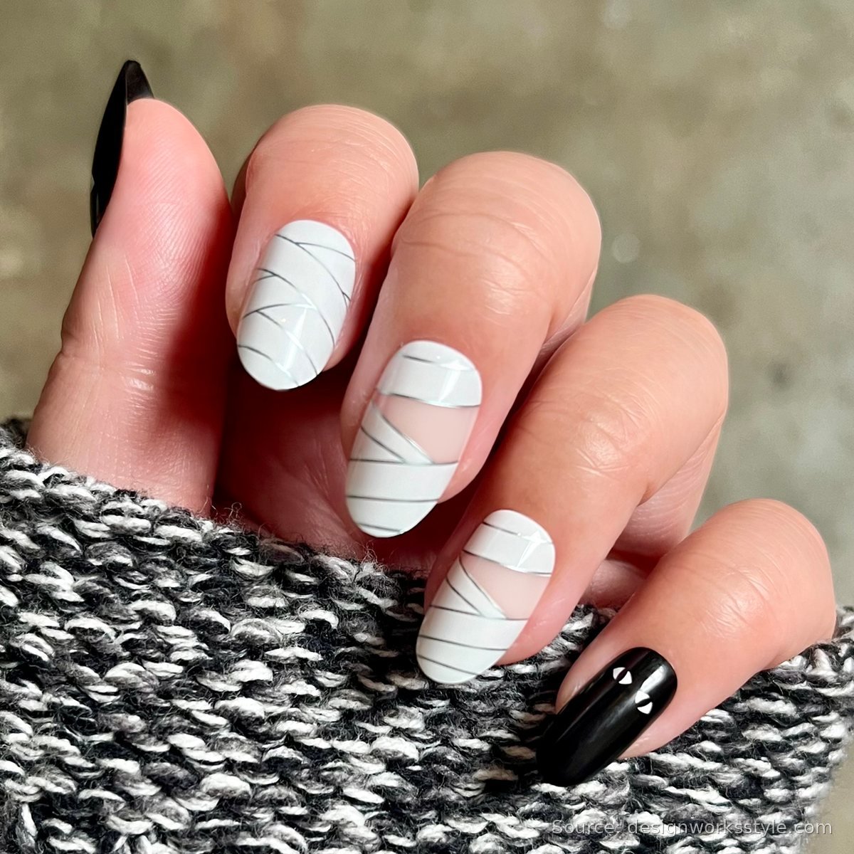 Mummy wrap Halloween nail art with white bandage stripes and black cat eye accent